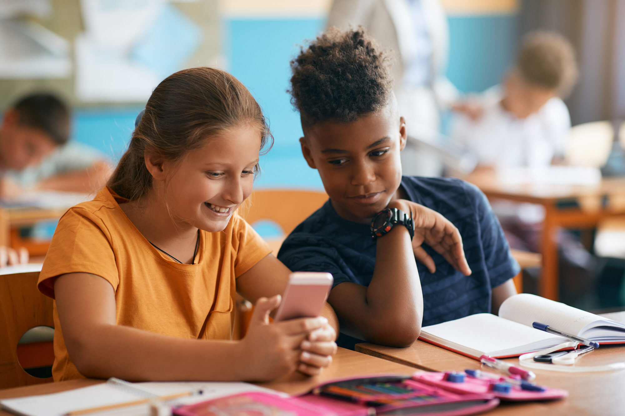 Happy classmates using cell phone in the classroom at elementary school.