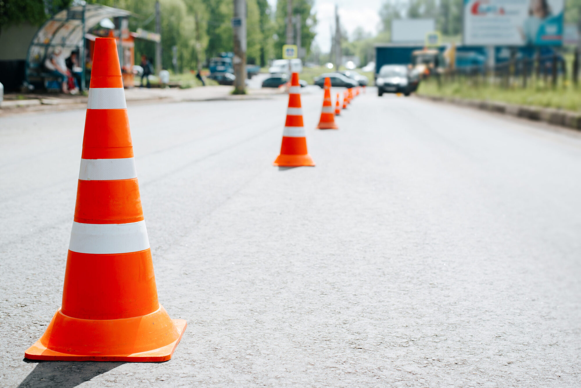 Traffic safety cones on asphalt of road. Selective focus on striped orange-white warning signs, cars bokeh