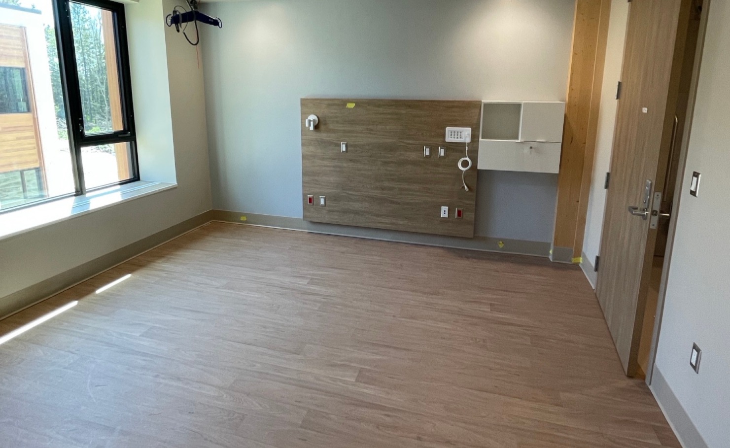 Une chambre d'hôpital neuve et vide, avec un plancher en bois clair.