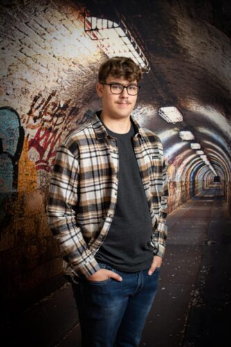Mathis Thériault, guide randonneur du PERO, chemise carottée, chandail noir, jeans, lunettes noires et chevelure rousse frisée, photo dans tunnel avec graffiti
