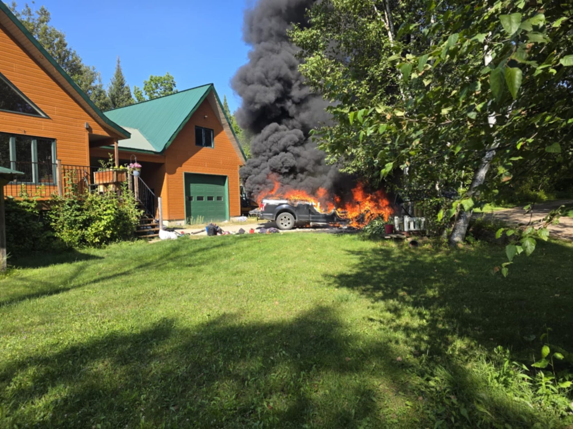 Des flammes s'échappent d'un véhicule en flamme devant une résidence de campagne.