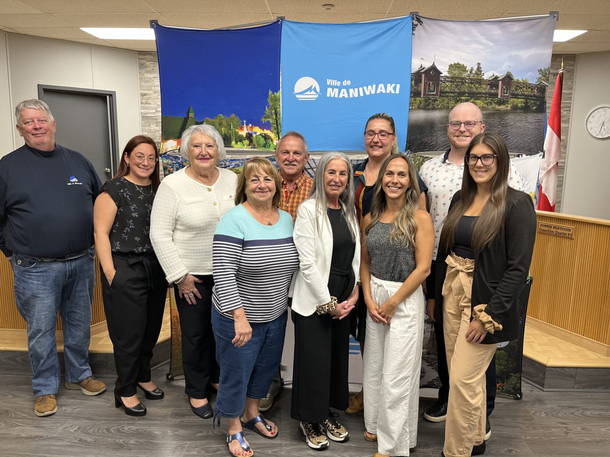 Un groupe de personnes prend la pause devant une affiche dans une salle municipale.