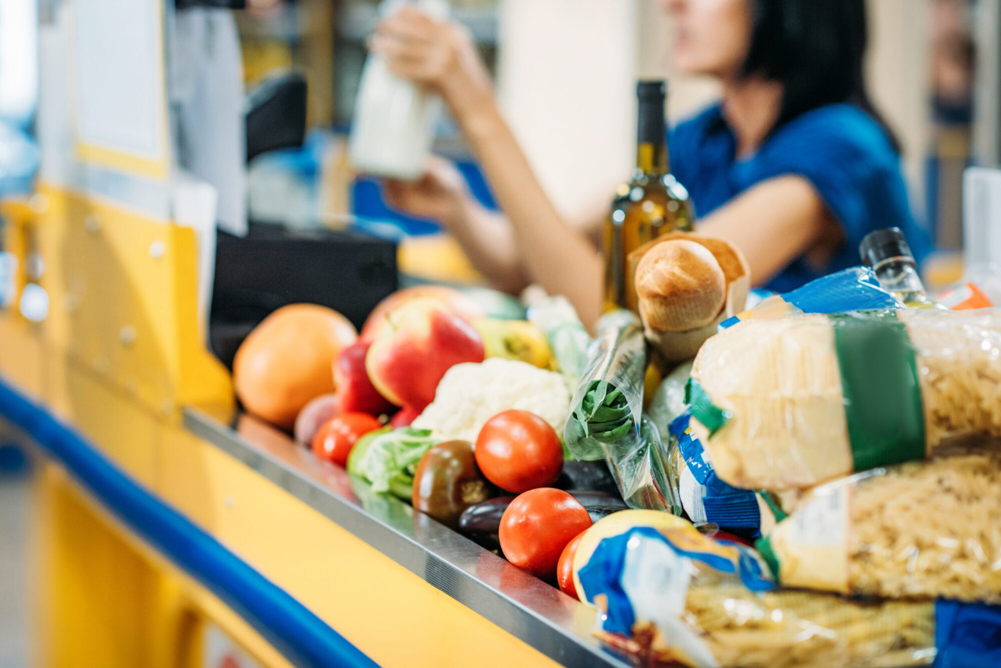 Des produits alimentaires sont posés sur le tapis roulant d'une caisse dans une épicerie.