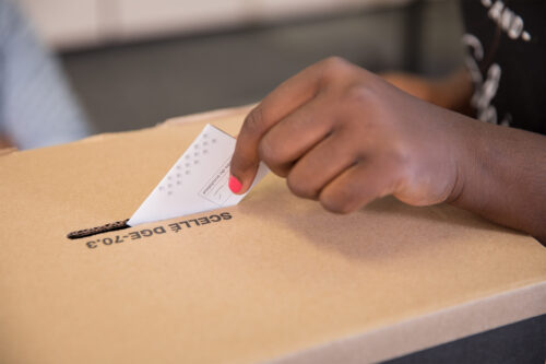 La main d'une personne noire glisse un bulletin de vote dans une urne.