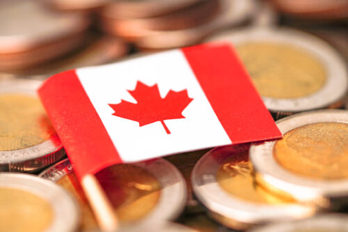 Un drapeau canadien est posé sur une pile de pièces de monnaie.