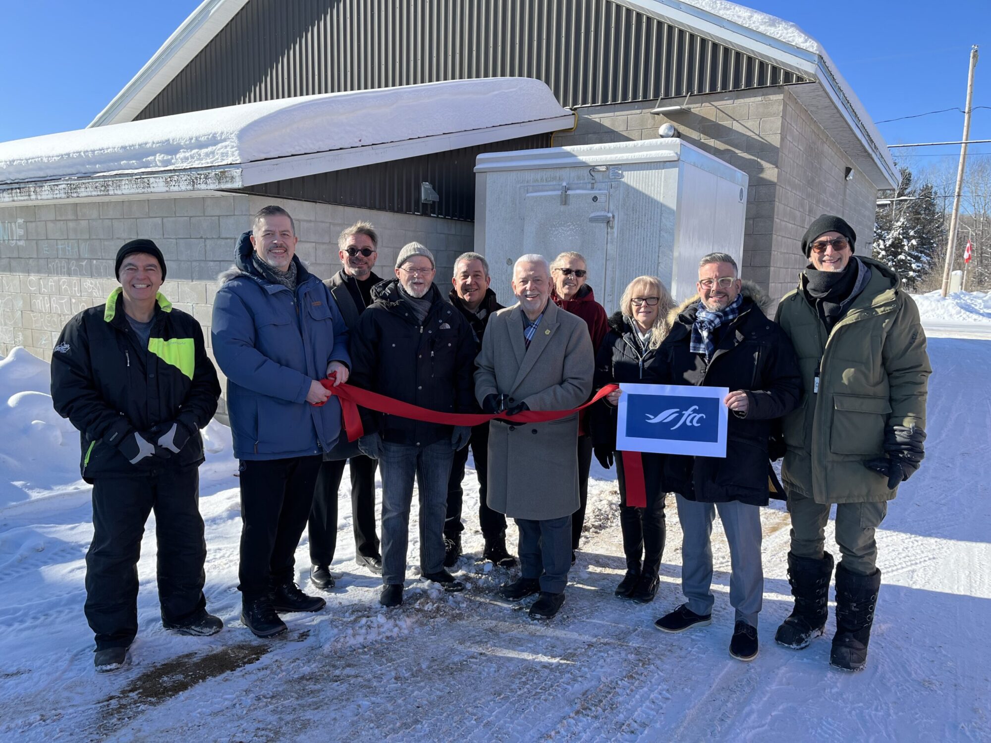 Un groupe de personnes procède à une coupure de ruban protocolaire près d'un bâtiment en hiver.