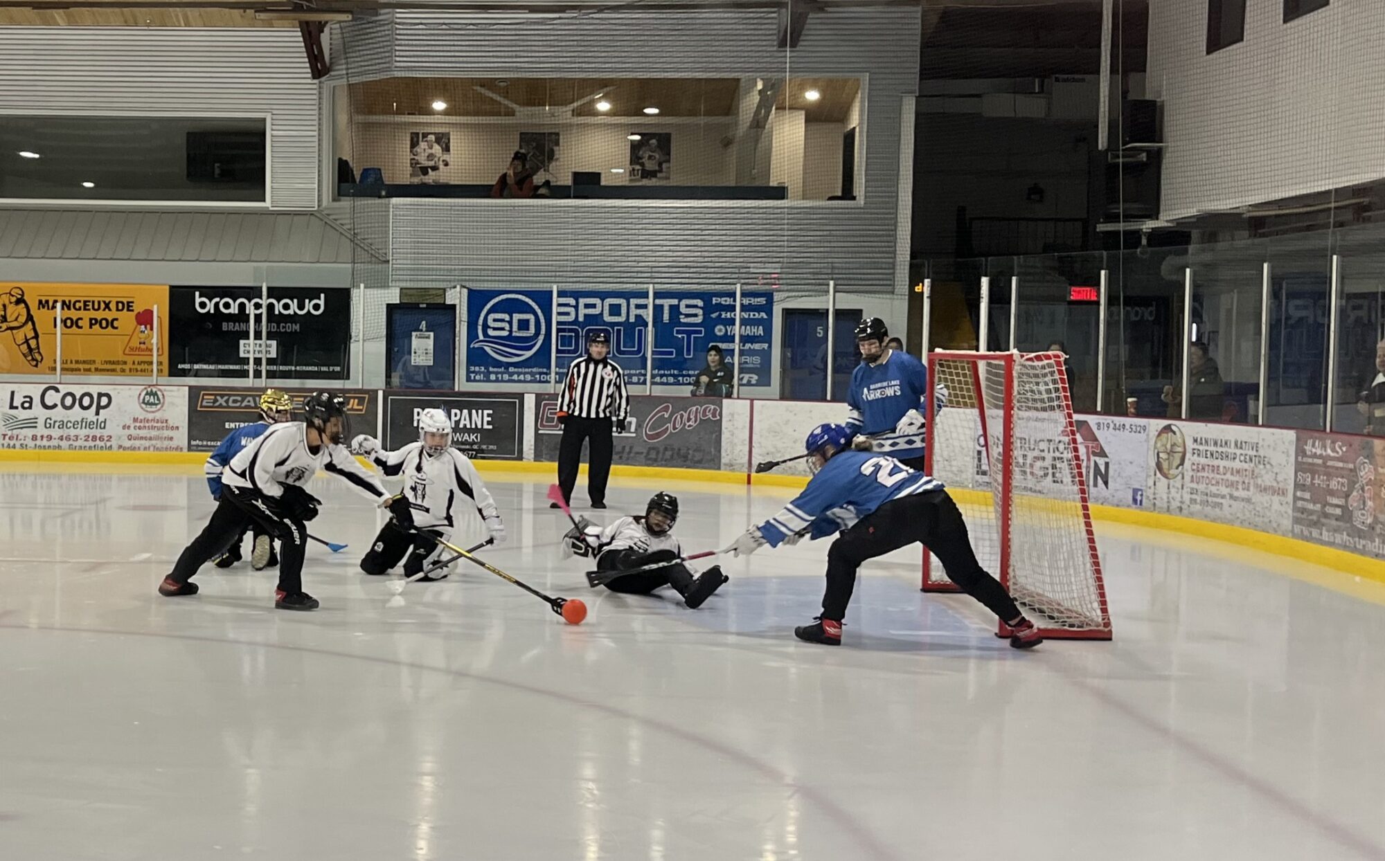 Des joueurs autochtones s'affrontent près d'un but lors d'une partie de ballon-balai dans un aréna.