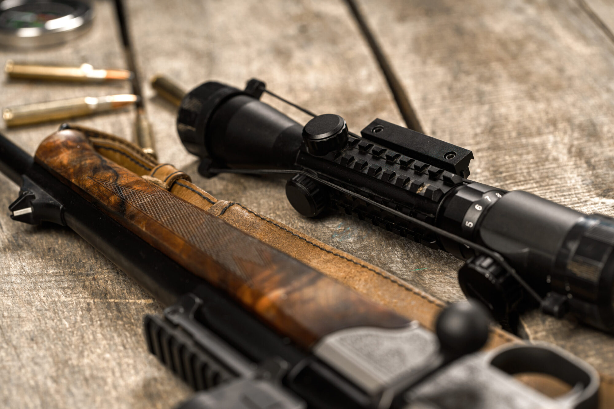 Un fusil de chasse, des cartouches et un viseur sont posés sur un support en planches de bois.