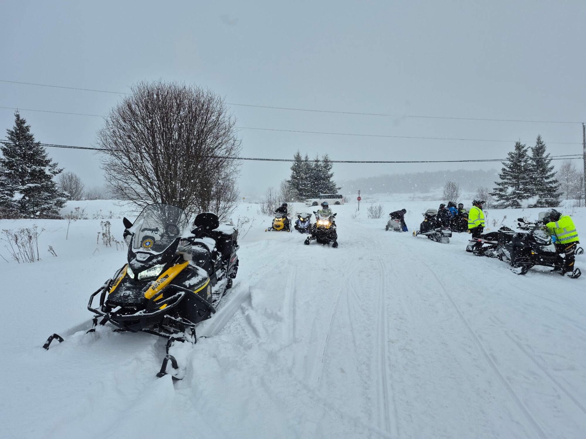 Des patrouilleurs de la Sûreté du Québec contrôlent des motoneigistes sur un sentier en plein hiver.
