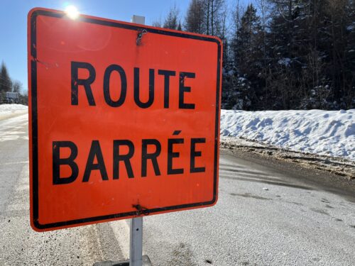 Un panneau routier orange posé au milieu d'une route en hiver indique que cette dernière est barrée à la circulation.