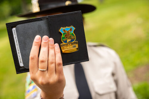 Une agente de protection de la faune du Québec brandit au premier plan son carnet d'identification avec le logo du ministère.