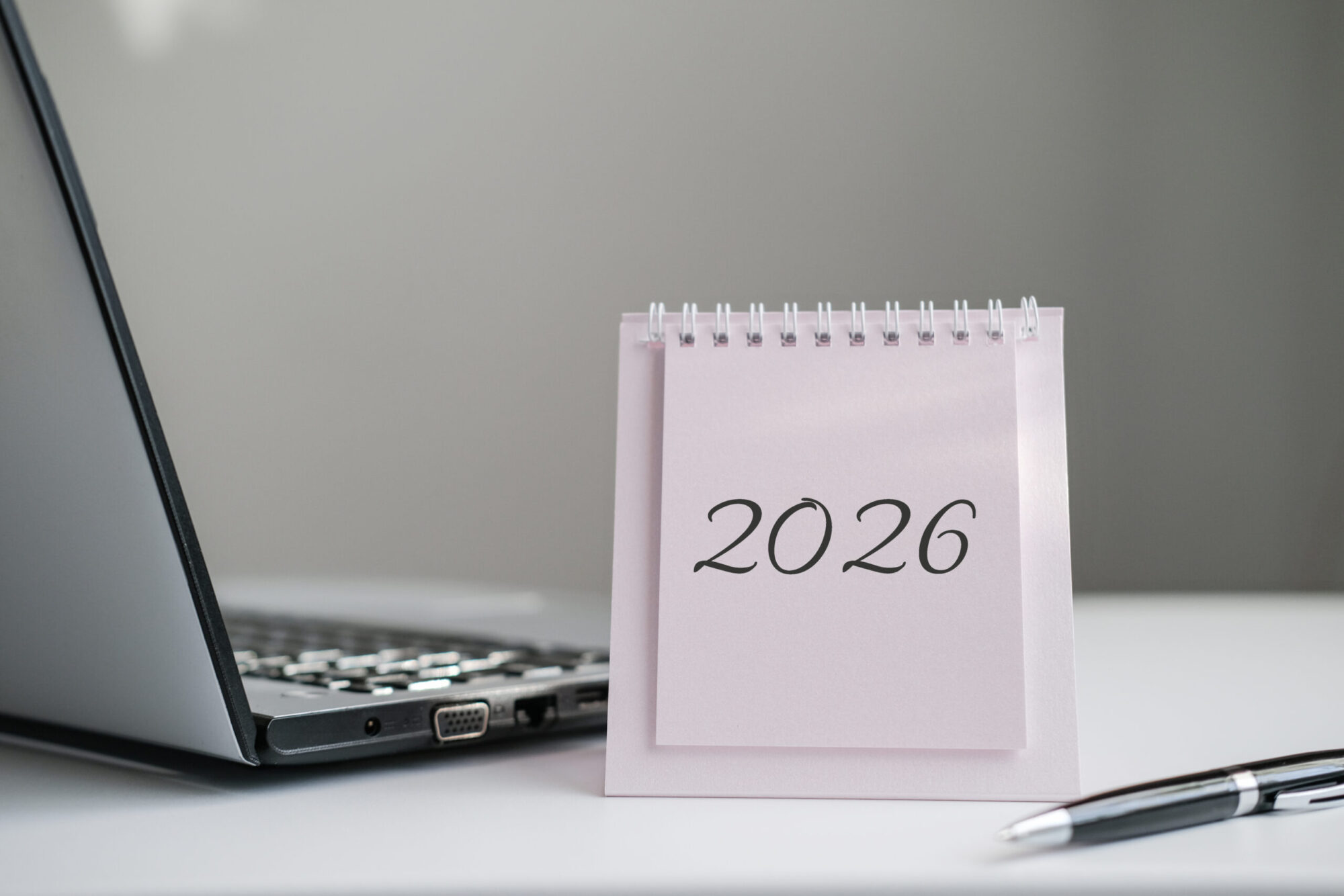 Calendar displaying "2026" is featured on desk next to laptop and pen. Great for themes of business, technology, and professional planning for the upcoming year
