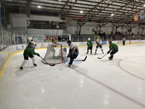 Des joueurs de hockey se disputent la rondelle près d'un but dans une aréna lors d'un match amateur.