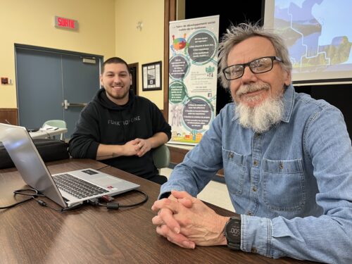 Deux hommes sont assis à une table lors d'une présentation publique.