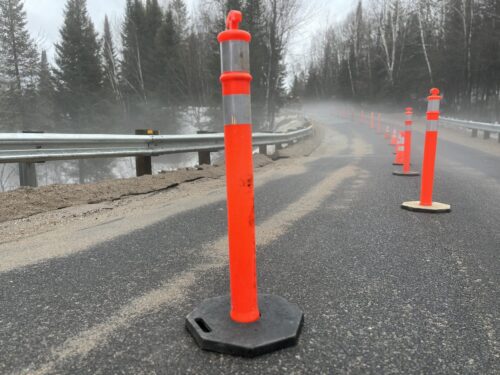 Des cônes orange sont placés sur la chaussée d'une route du Québec encadrée par des glissières de sécurité. La saison est le printemps. Le temps est pluvieux et la neige est en train de fondre.