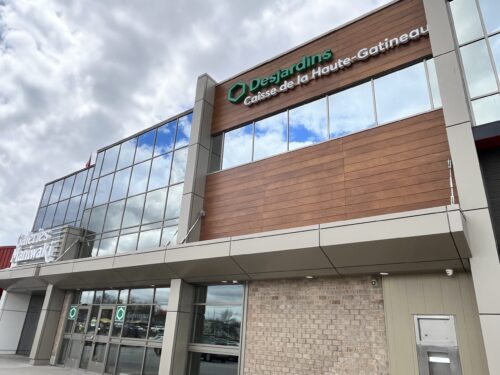 La façade d'un bâtiment intégré à un centre commercial sur lequel on voit le logo de la Caisse populaire Desjardins.