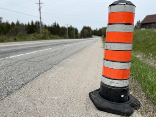 Un cône orange de chantier est posé en bordure d'une route rurale du Québec.