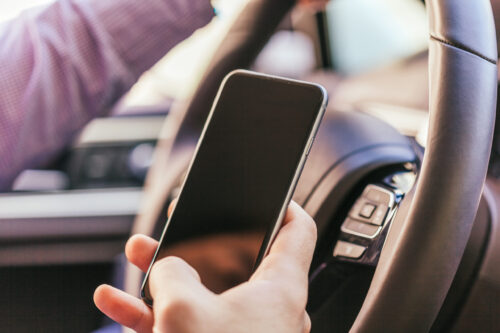 Un homme en train de conduire tient son téléphone cellulaire dans sa main droite.