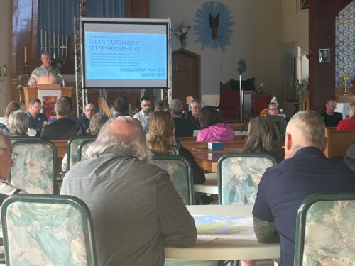 consultation à l'église de Blue Se avec gens assis à des tables et tournés vers l'avant, regardant un homme expliquant l'information dévoilée sur un écran blanc