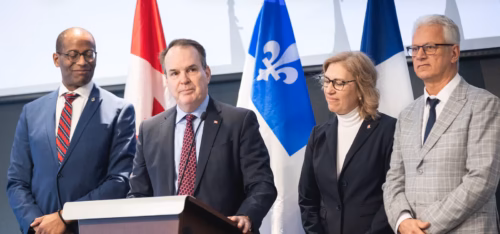 Députés fédéraux de l'Outaouais, Greg Fergus (Hull-Aylmer), Steven McKinnon (Gatineau), Sophie Chatel (Pontiac—Kitigan Zibi) et Stéphane Lauzon (Argenteuil—La Petite-Nation), devant public avec drapeaux du Québec et Canada derrière eux, debouts et devant un lutrin