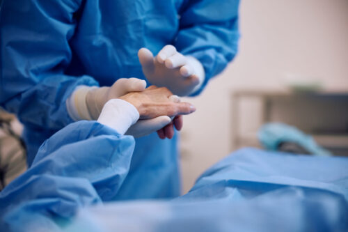 Un membre d'une équipe médicale prend la main d'une patiente allongée pour une chirurgie dans la sienne.