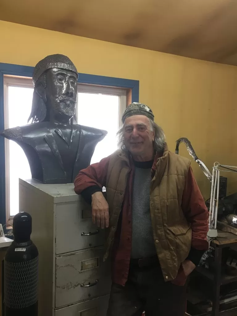 Donald-Doiron-et-une-de-ses-sculpures-rendant-hommage-à-Joseph-Beausoleil-Brossard-768x1024