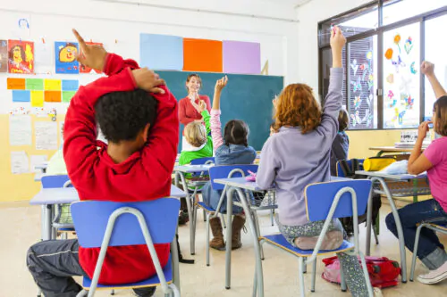 Rear view of primary schoolgirls and boys with hands raised in classroom