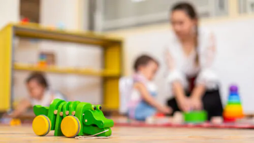 Closeup of wooden crocodile toy and kids playing with toys in the background