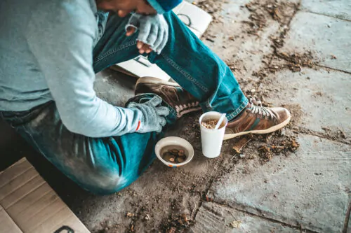 Begging under the bridge with a cup containing coins and instant