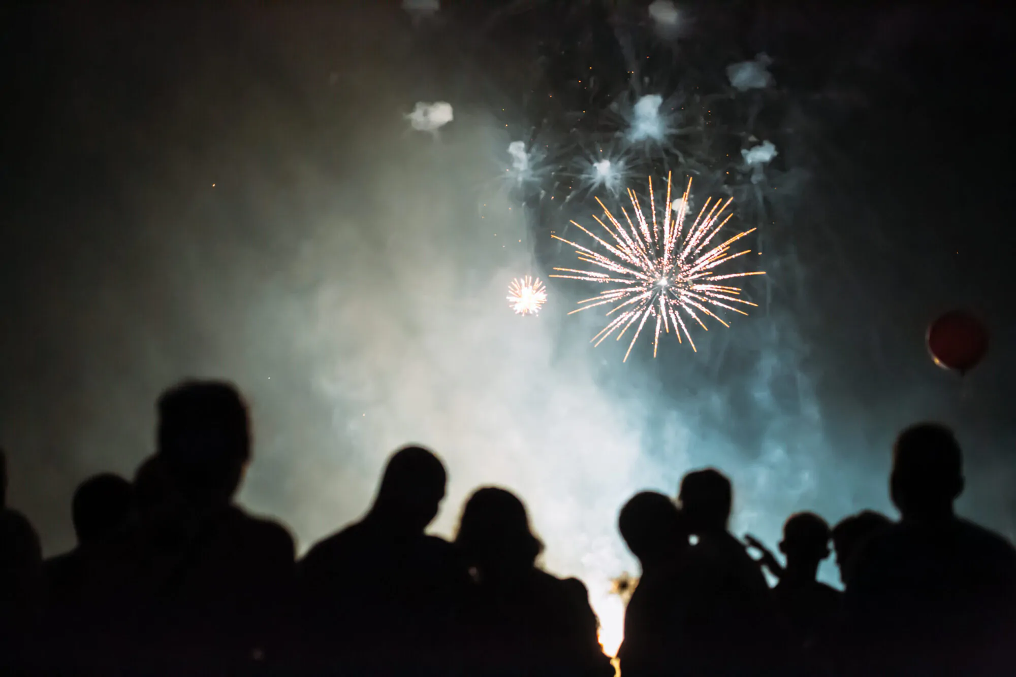 Une foule dans l'ombre assiste à l'explosion de feux d'artifice dans la nuit.