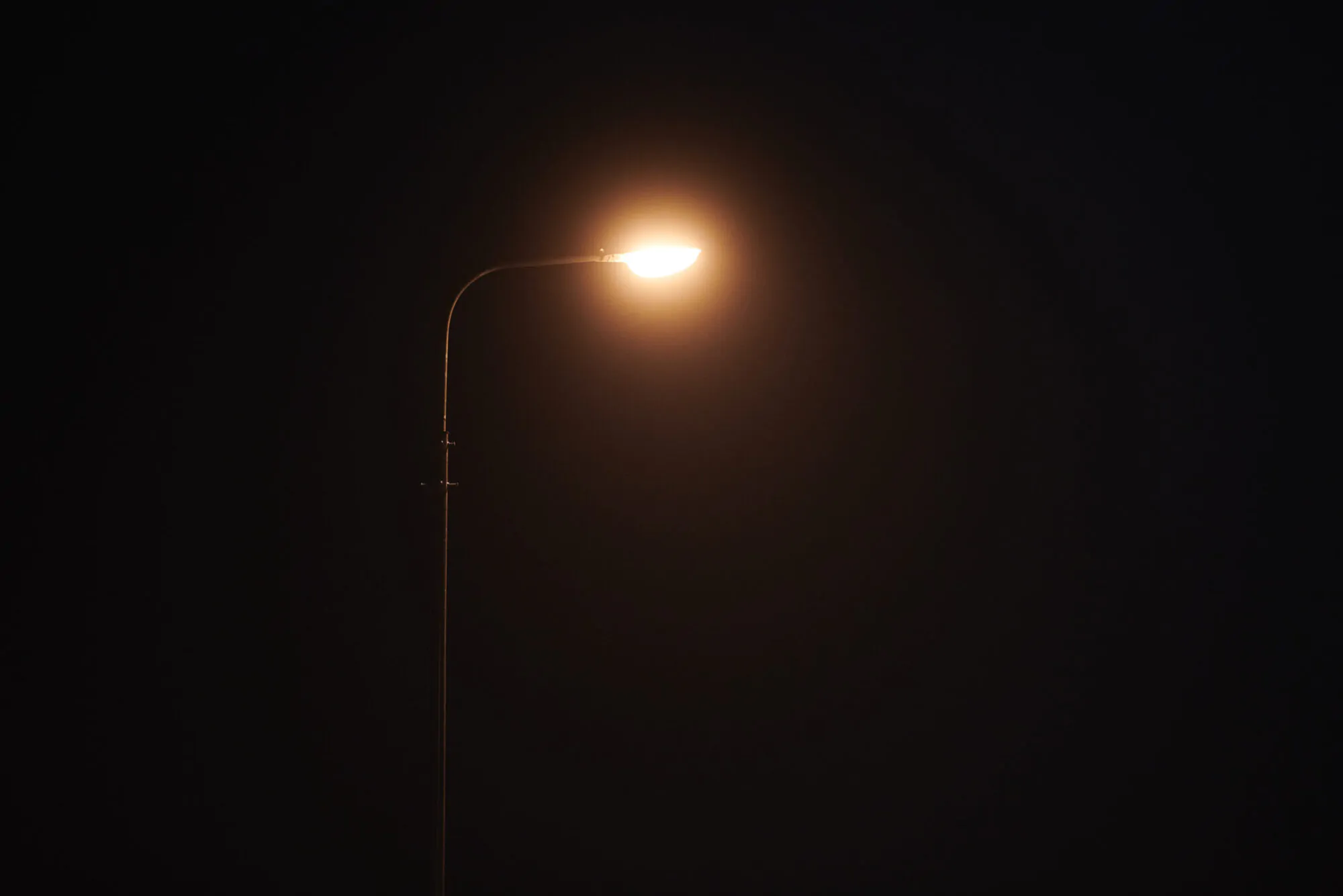 One night lamppost shines with faint mysterious yellow light through evening fog, copy space