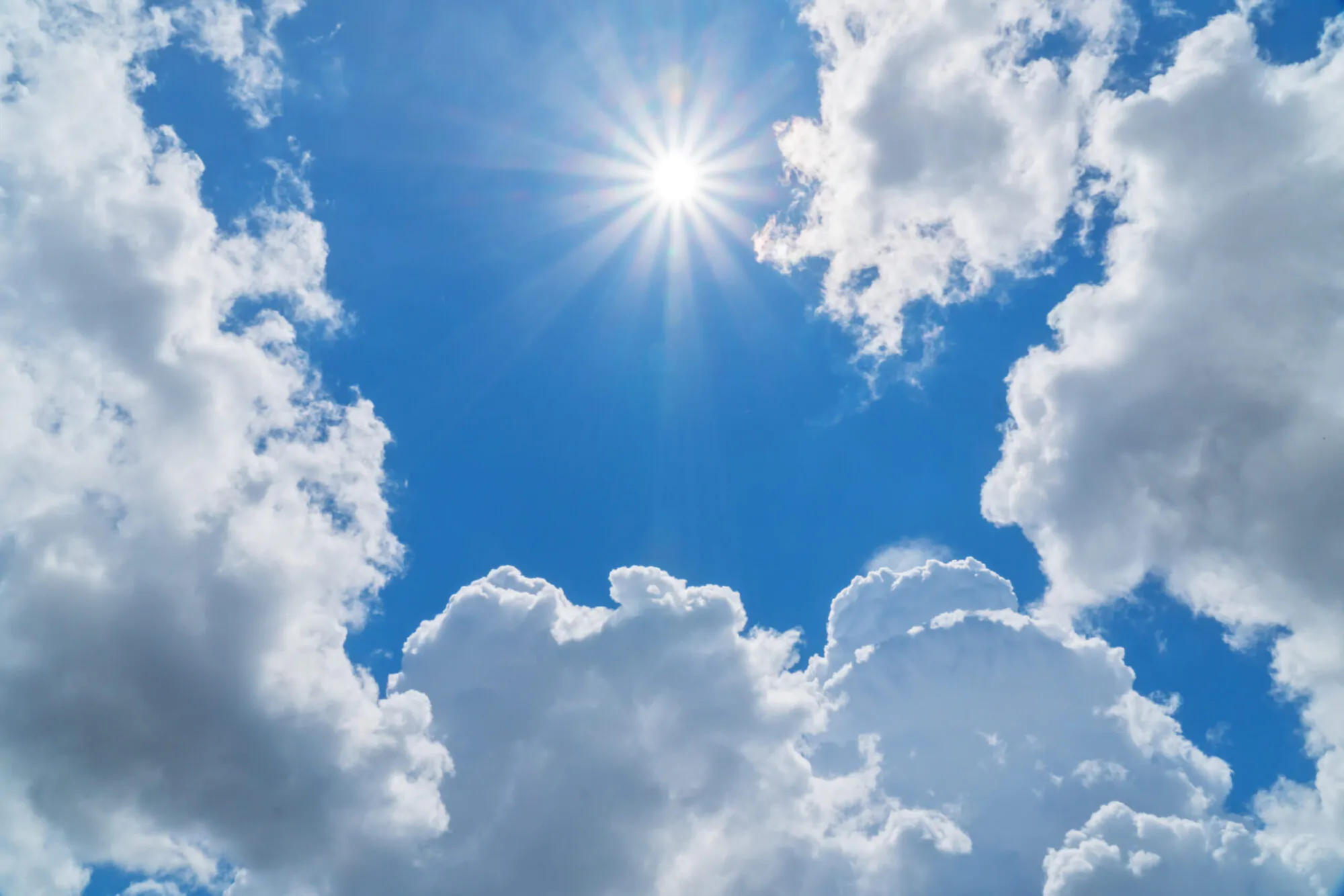 Un grand soleil brille au milieu d'un ciel bleu et de nuages blancs.