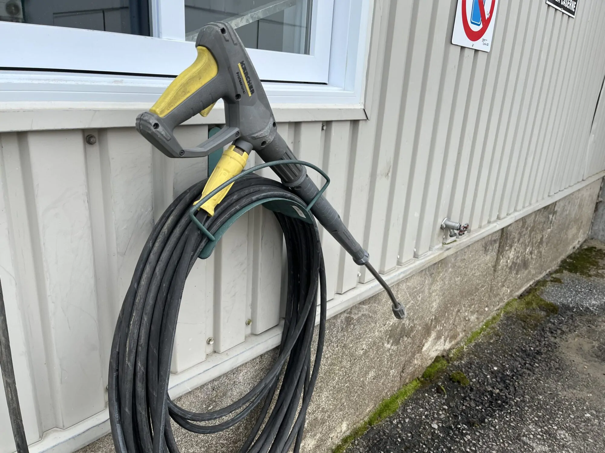 Une hausse à pression enroulée le long d'un bâtiment beige, sous une fenêtre blanche.