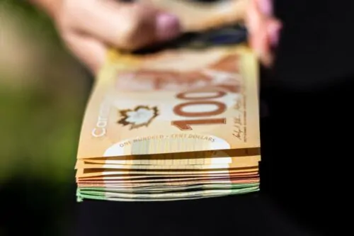 Gros plan sur des liasses de billets de 100$ et de 20$ canadiens tenus dans des mains.