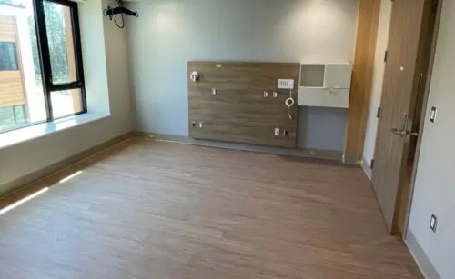 Une chambre d'hôpital neuve et vide, avec un plancher en bois clair.