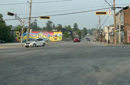 Une voiture blanche tourne à droite sur une rue à une intersection dans une ville, un soir d'été avec un ciel dégagé. Une autre voiture rouge s'arrête, alors que les feux de circulation aux quatre coins d'une intersection sont éteints.