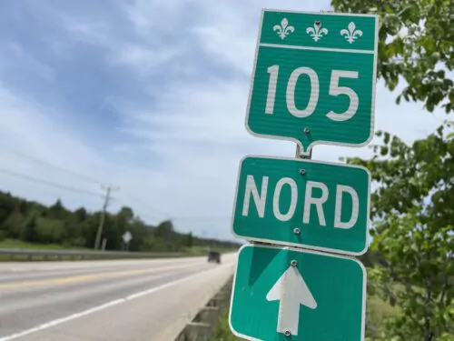 Un panneau routier du Québec planté au bord de la route 105 en été indique avec une flèche la direction nord.