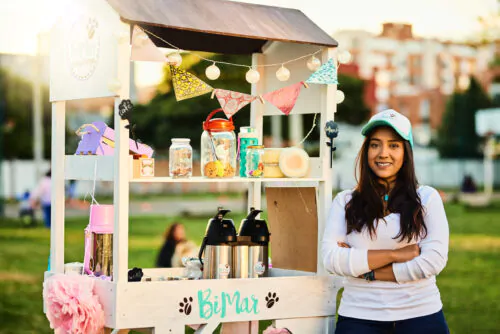 Adolescente avec casquette blanche et cheveux longs bruns, kiosque extérieur en bois, limonade, thé glacé à vendre