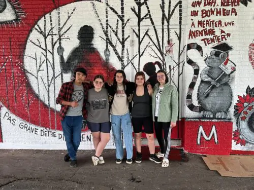 Groupe de jeunes étudiants devant une murale extérieure peinte eb noir, rouge, blanc et gris