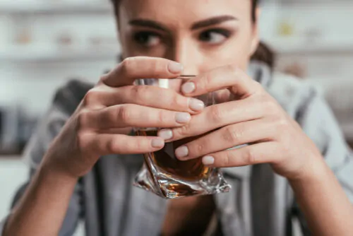 Une femme regarde sur le côté en tenant dans ses mains un verre d'alcool.