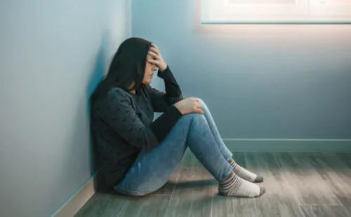 Une femme qui semble en détresse est assise dans le coin d'une pièce et se tient la tête dans la main.
