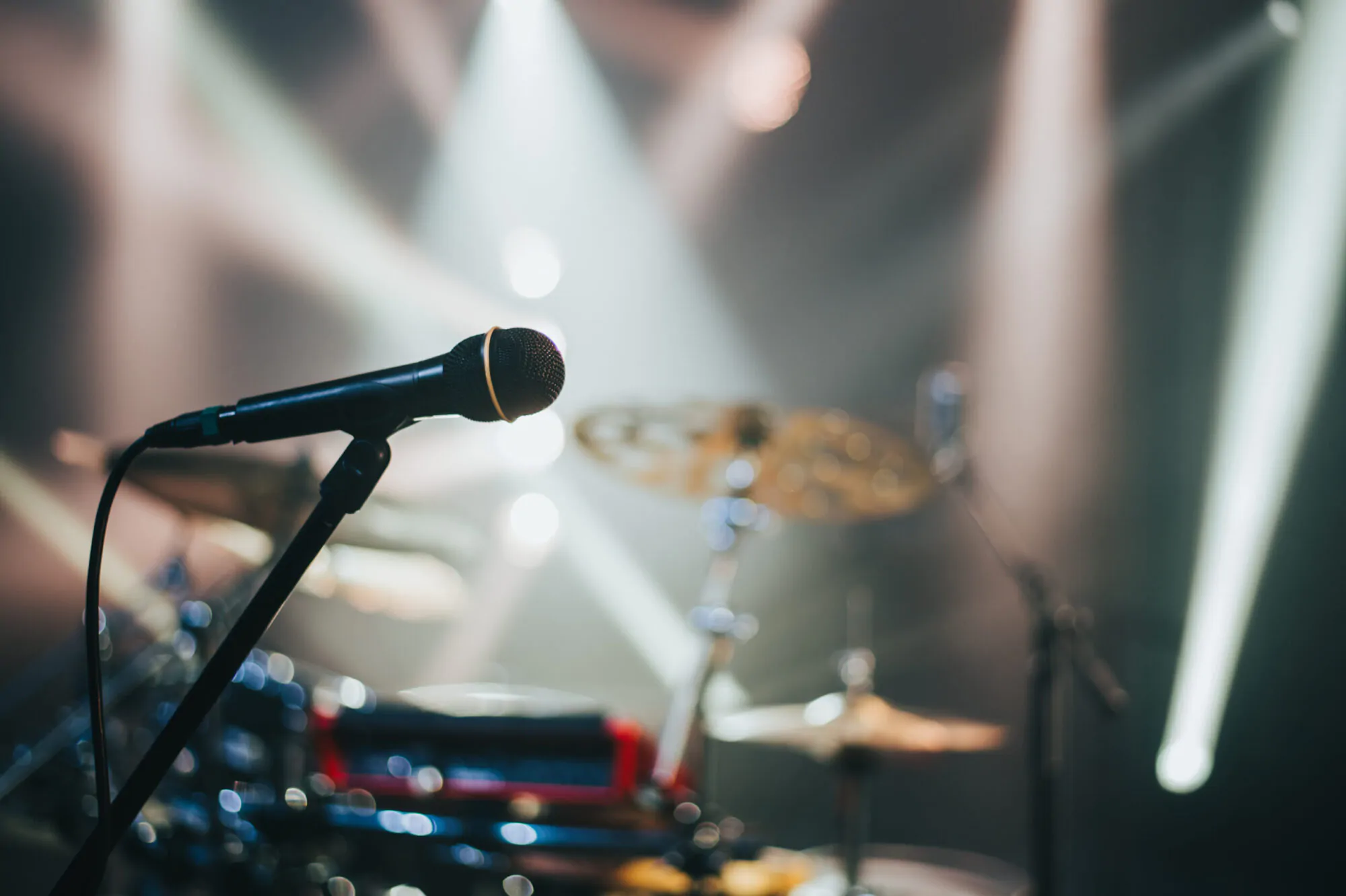 Gros plan sur un micro posé sur une scène de spectacle avec des cymbales en arrière-plan et des néons.
