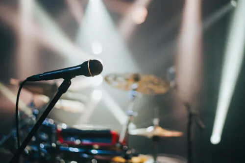 Gros plan sur un micro posé sur une scène de spectacle avec des cymbales en arrière-plan et des néons.