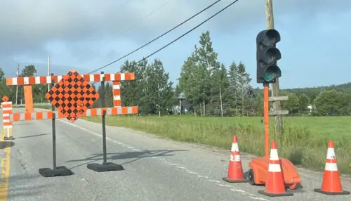 Un feu de circulation est posé sur le bord d'une route avec des cônes orange autour. De la signalisation routière orange indique l'entrée sur un chantier en été.