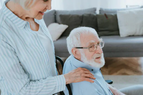 homme âgé dans chaise berçante et femme auprès de lui avec main sur son épaule