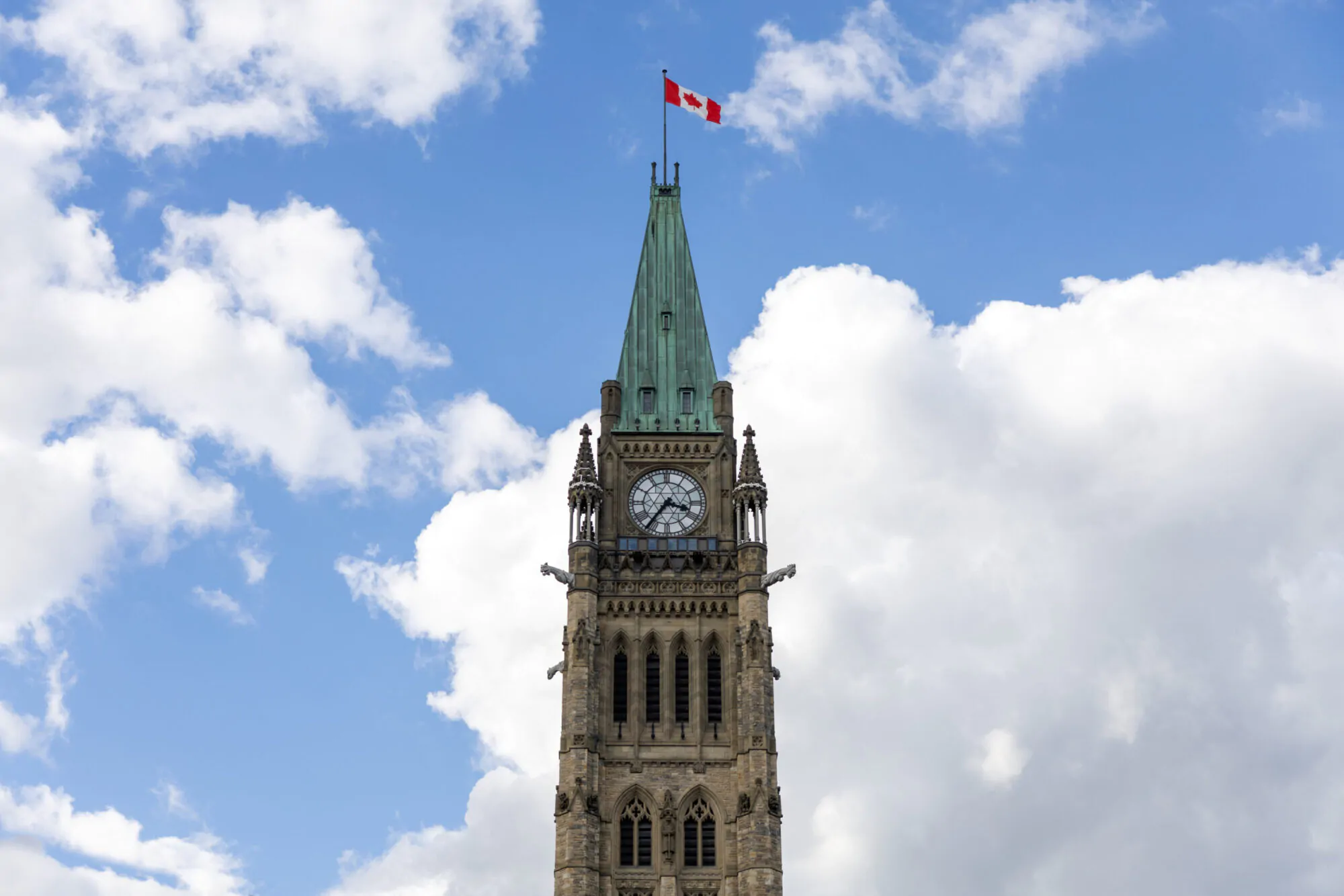 Une tour du parlement canadien à Ottawa avec un drapeau du Canada qui flotte au sommet sur un ciel bleu et ennuagé.