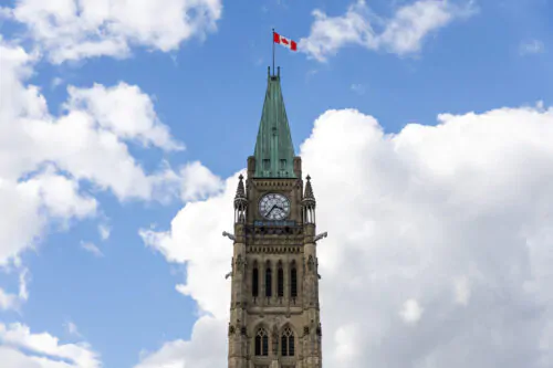 Une tour du parlement canadien à Ottawa avec un drapeau du Canada qui flotte au sommet sur un ciel bleu et ennuagé.