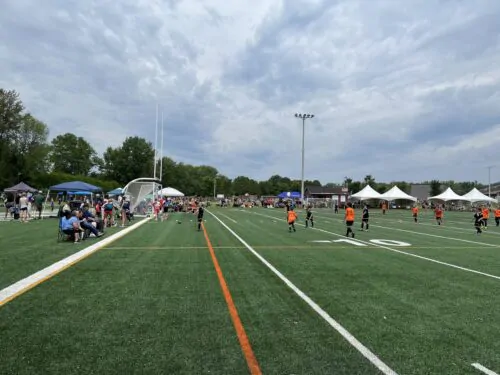 De jeunes joueurs de soccer habillés en orange et en noir s'affrontent sur un terrain de soccer sous les yeux d'une foule.