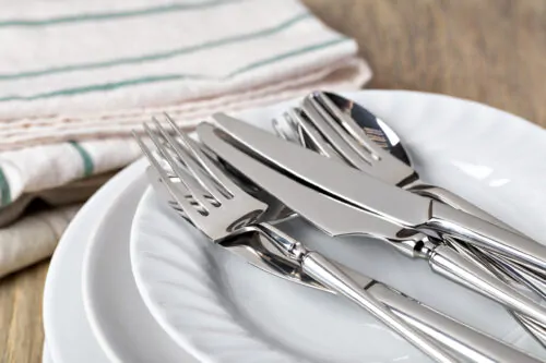 Des fourchettes et des couteaux sont posés sur une pile d'assiettes blanches, avec des serviettes à côté.
