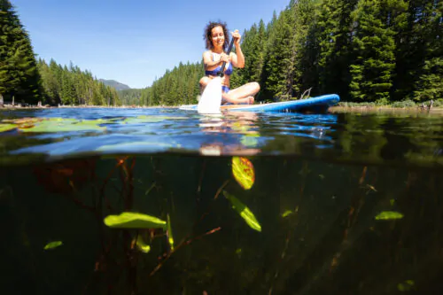 Une femme en maillot de bain pagaye en étant assise sur une planche à pagaie sur un plan d'eau au Canada.